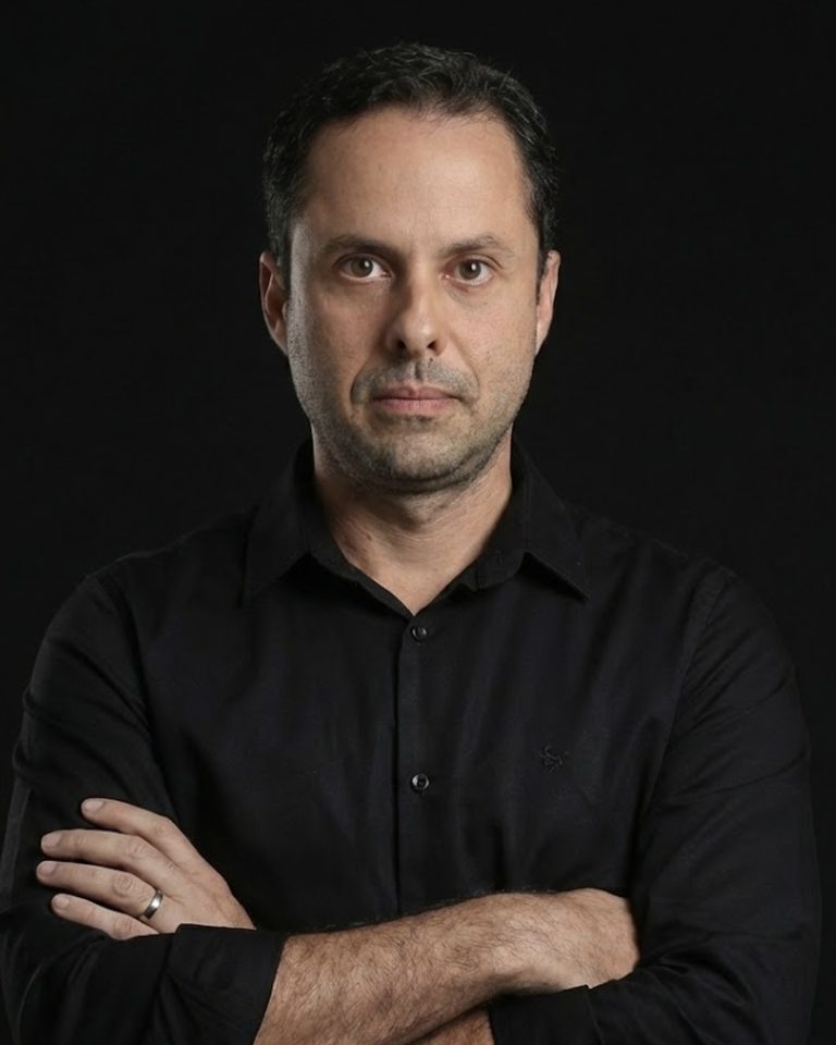 Fernando Saback de Freitas, palestrante do curso, de braços cruzados em fundo escuro